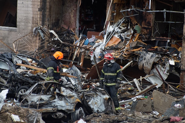 a couple of firemen standing next to a pile of rubble