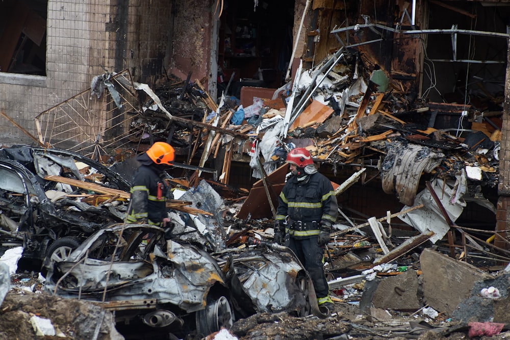 a couple of firemen standing next to a pile of rubble