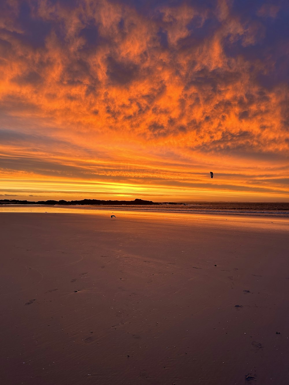 a sunset view of a beach with footprints in the sand