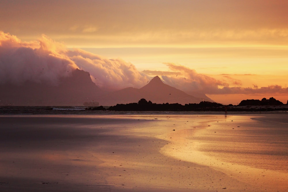 une vue du coucher de soleil d’une plage avec une montagne en arrière-plan