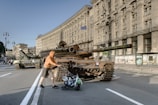a man pushing a stroller past a tank on the street
