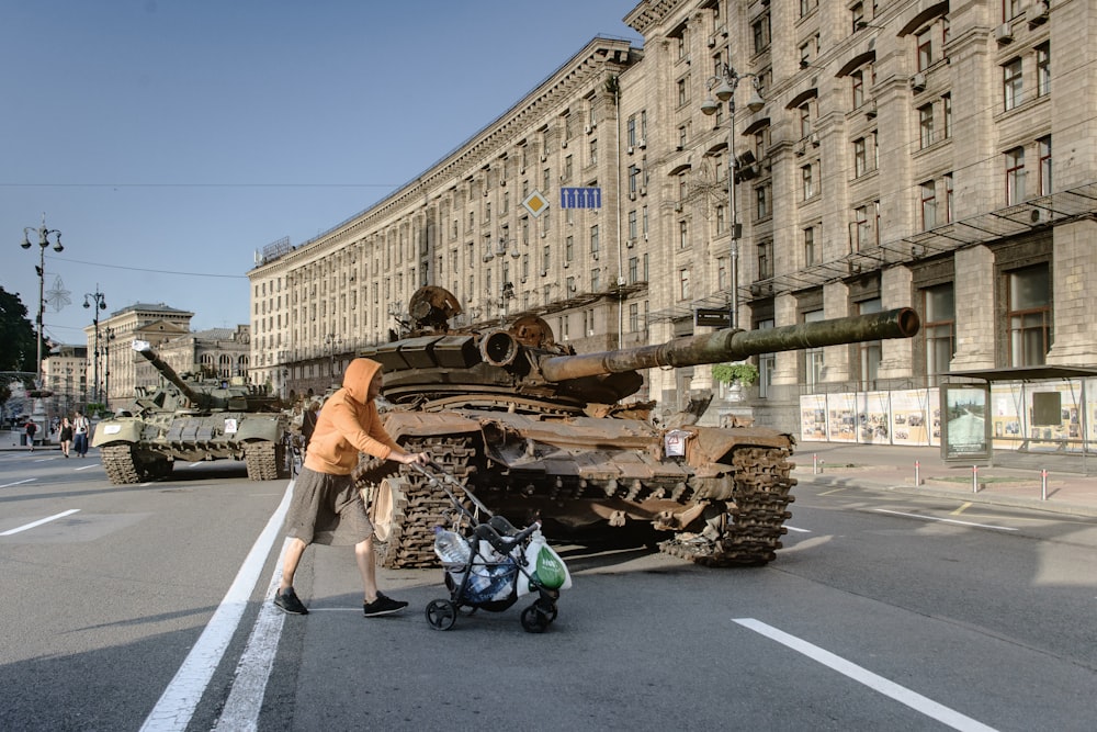 a man pushing a stroller past a tank on the street