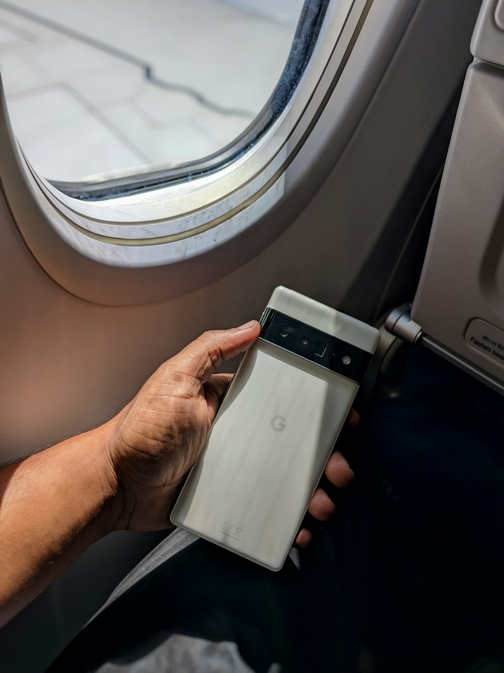 a person holding a cell phone next to an airplane window