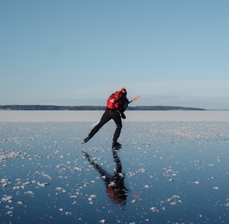 a man in a red jacket is ice skating on a sea or lake