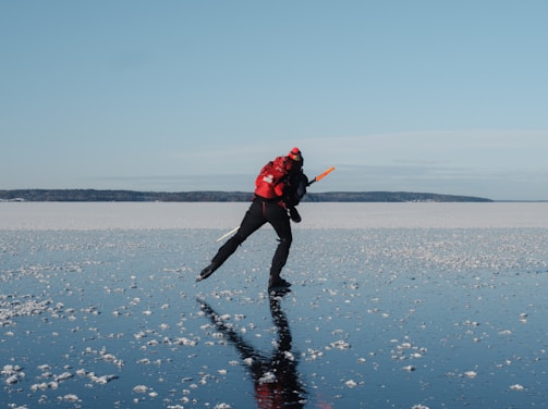 a man in a red jacket is ice skating on a sea or lake