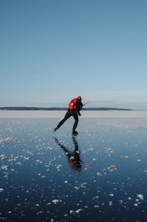 a man in a red jacket is ice skating on a sea or lake