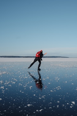 a man in a red jacket is ice skating on a sea or lake