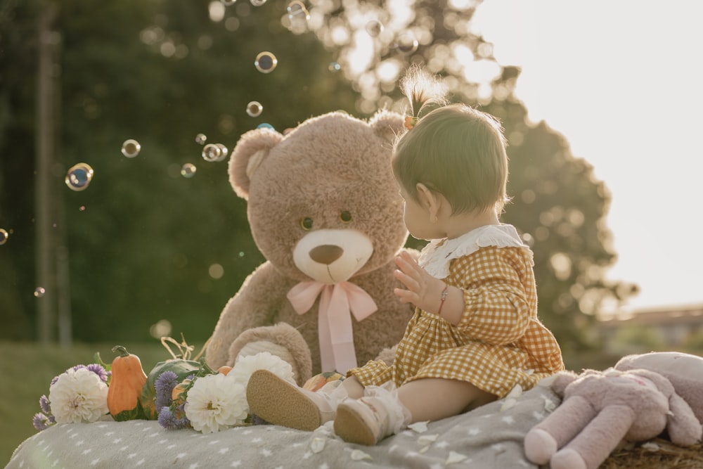 a little girl sitting on a blanket next to a teddy bear