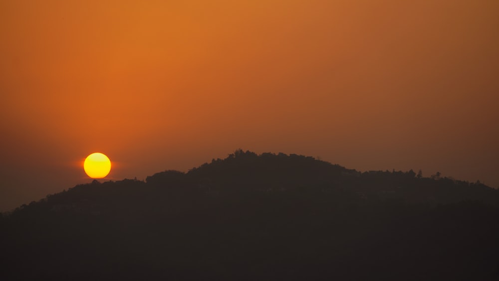 the sun is setting over a hill with trees