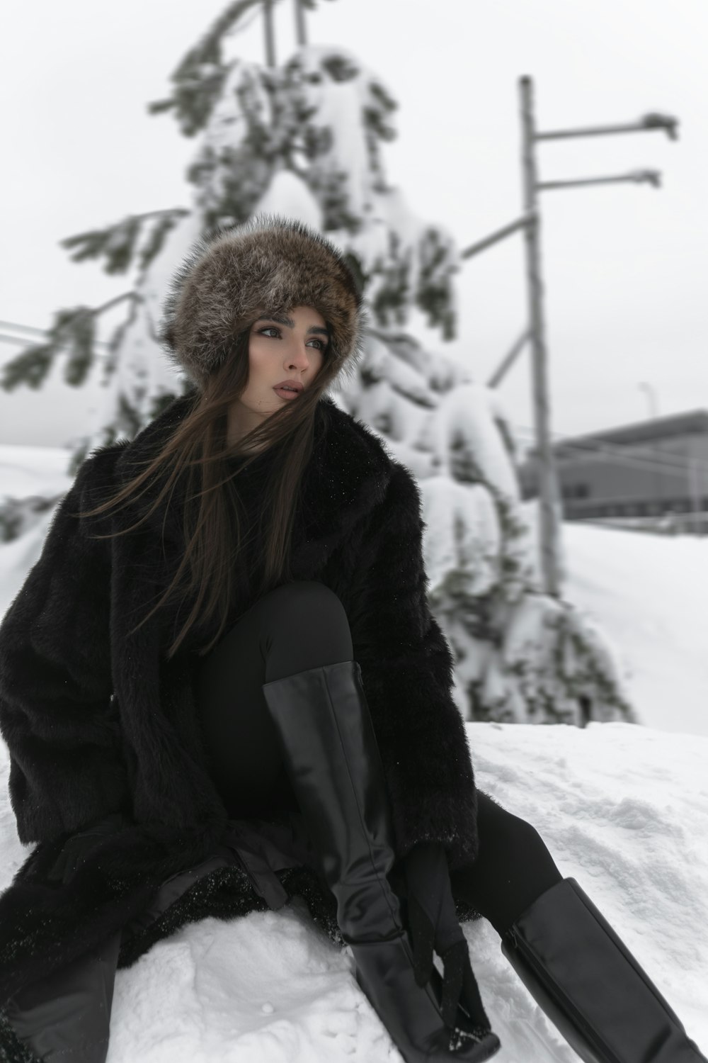 a woman sitting in the snow wearing a fur hat