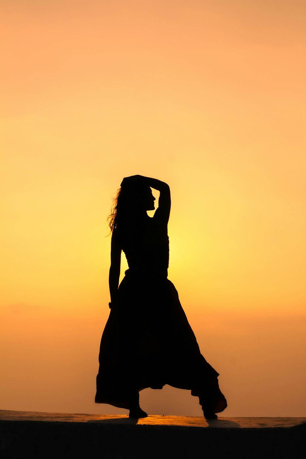 eine Frau in einem langen Kleid tanzt bei Sonnenuntergang am Strand