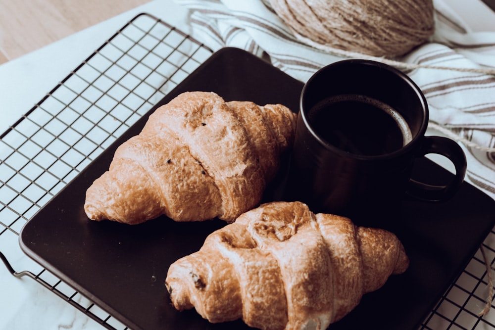 two croissants on a black plate next to a cup of coffee