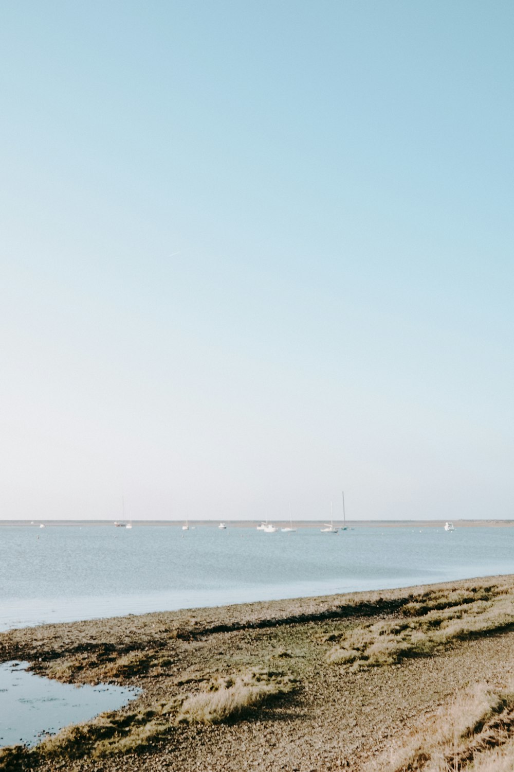 a beach with a body of water and boats in the distance