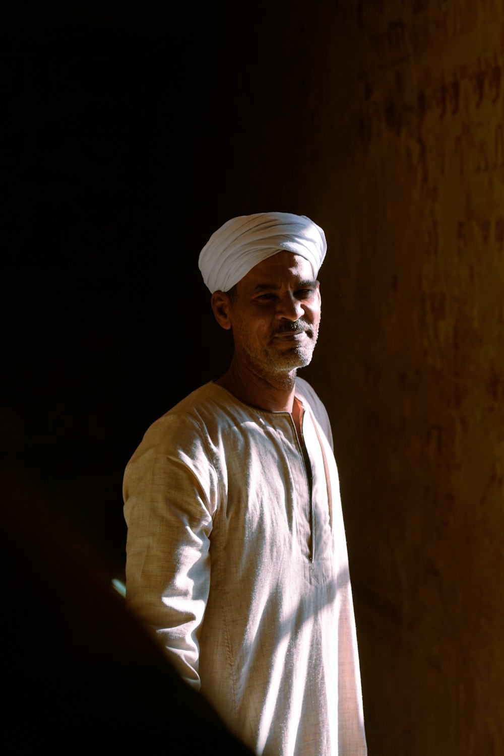 a man with a white turban standing in a dark room