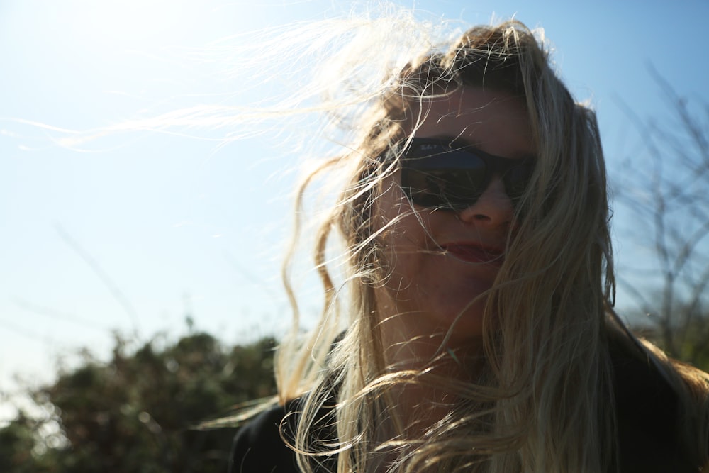 a woman with sunglasses on her face and hair blowing in the wind