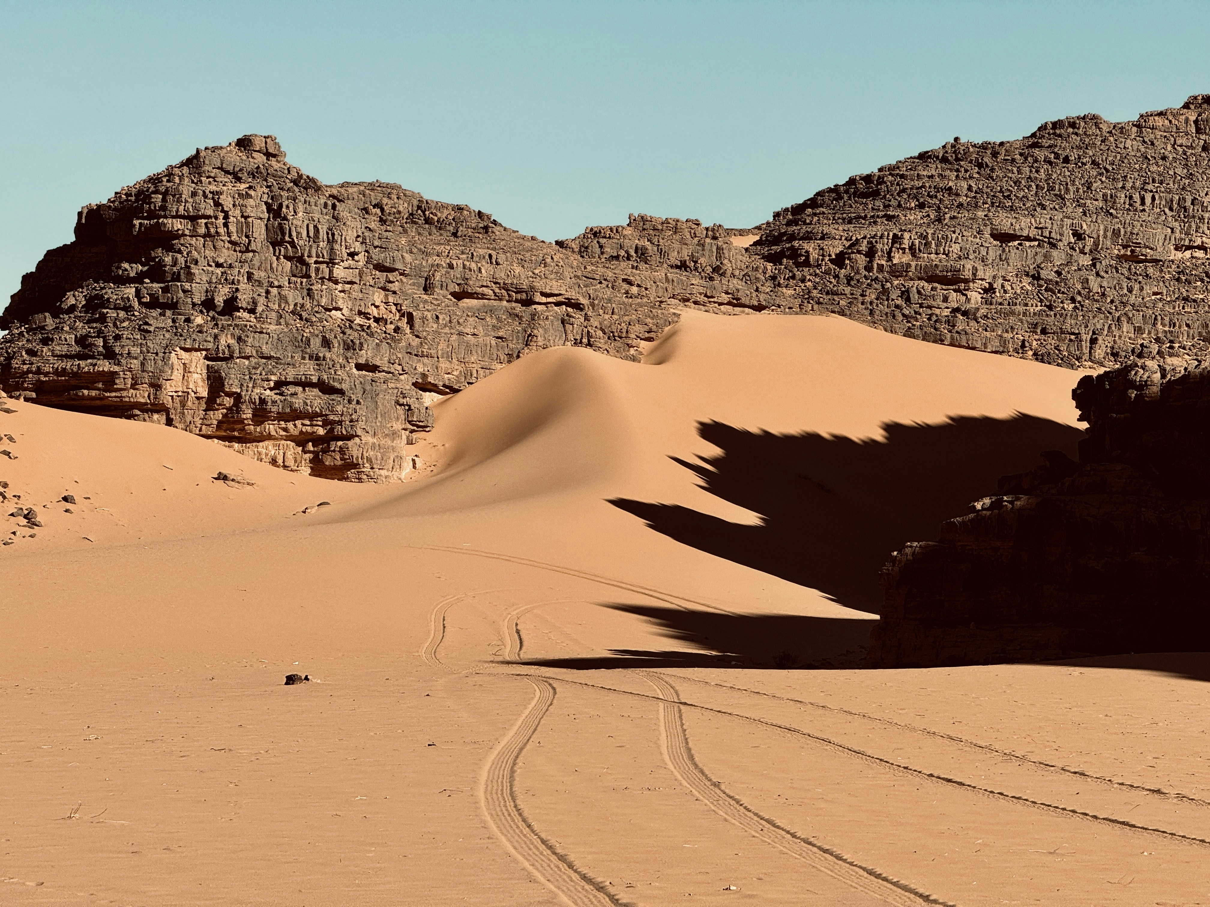 a desert landscape with a rock formation and tracks in the sand