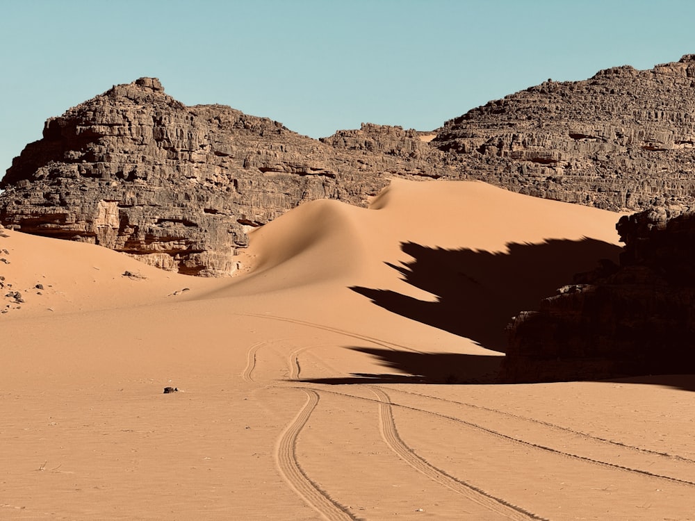 a desert landscape with a rock formation and tracks in the sand