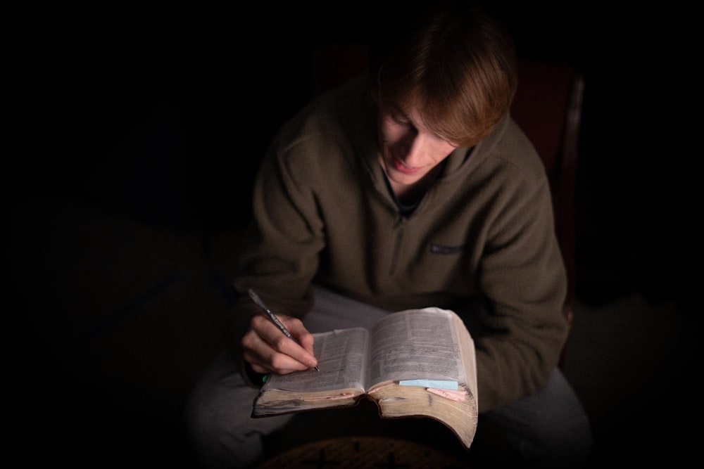 a man sitting in a chair holding a book and a pen