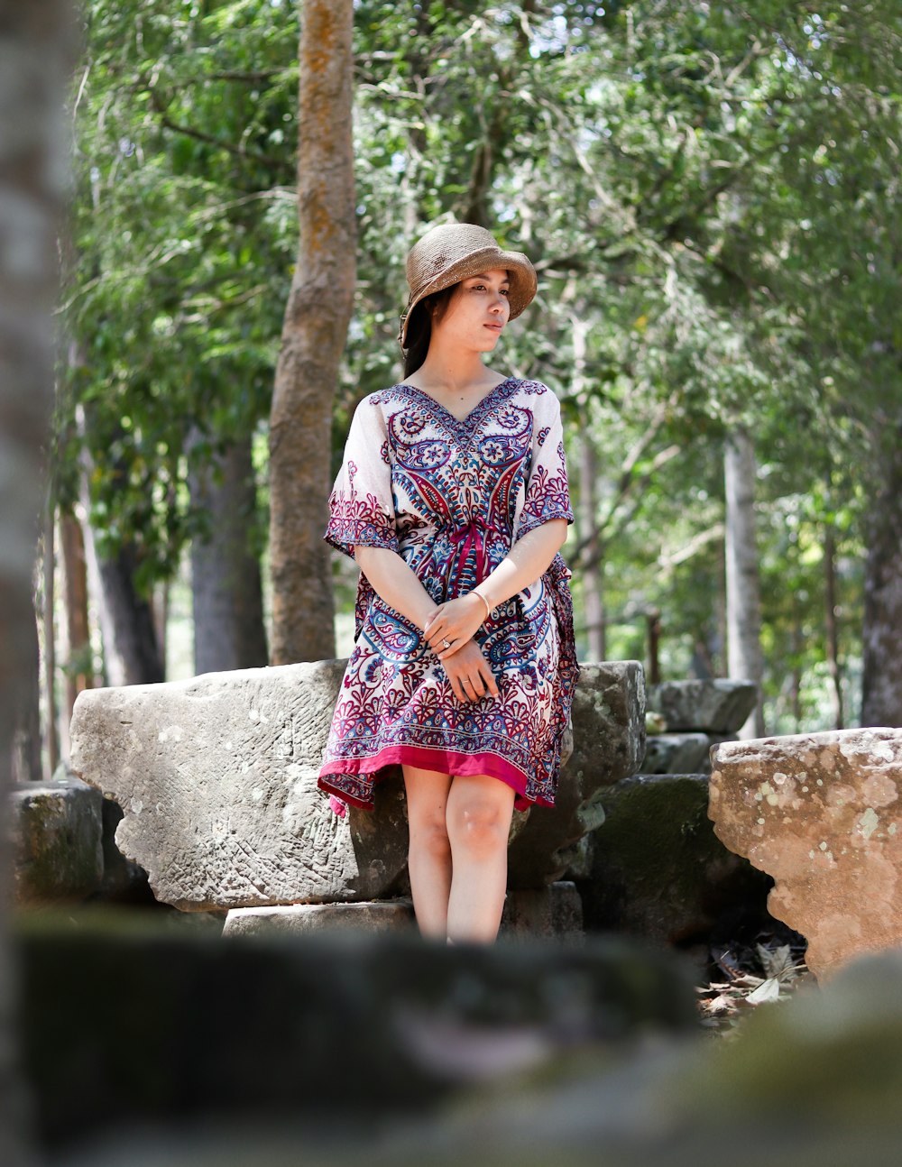 a woman in a dress and hat sitting on a rock