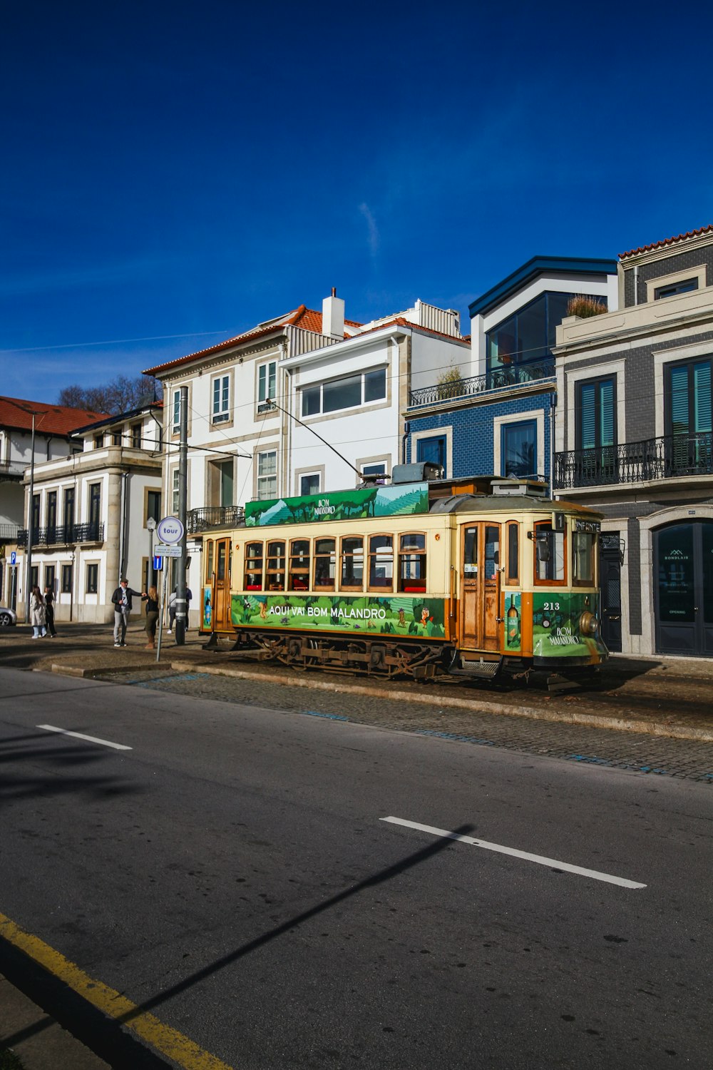 a green and yellow train traveling past tall buildings