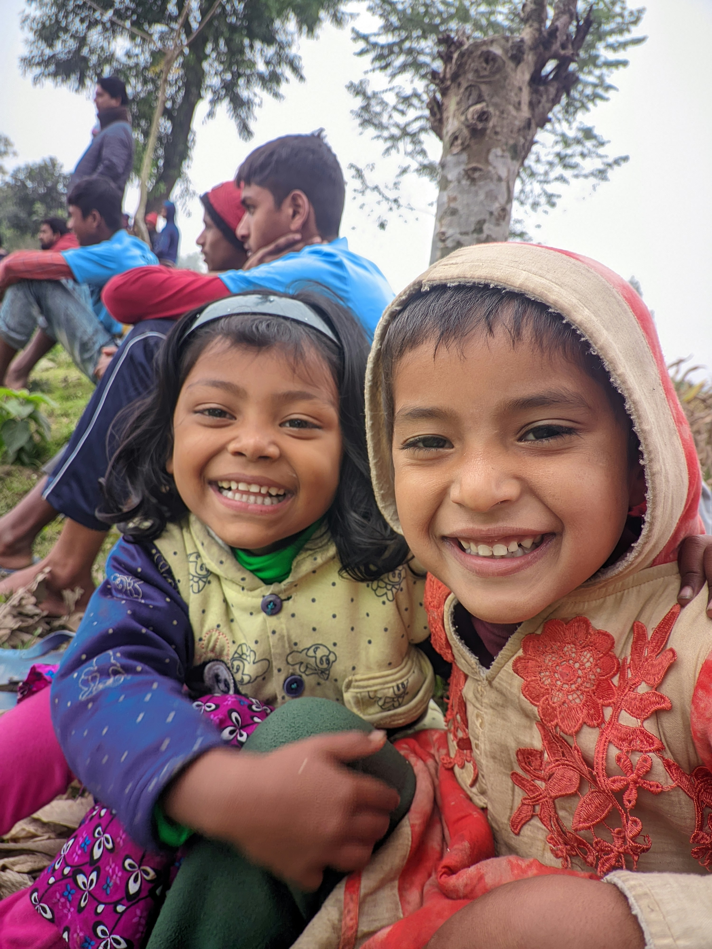 Child smiling while receiving new clothes from volunteer, warm outdoor light, joyful moment