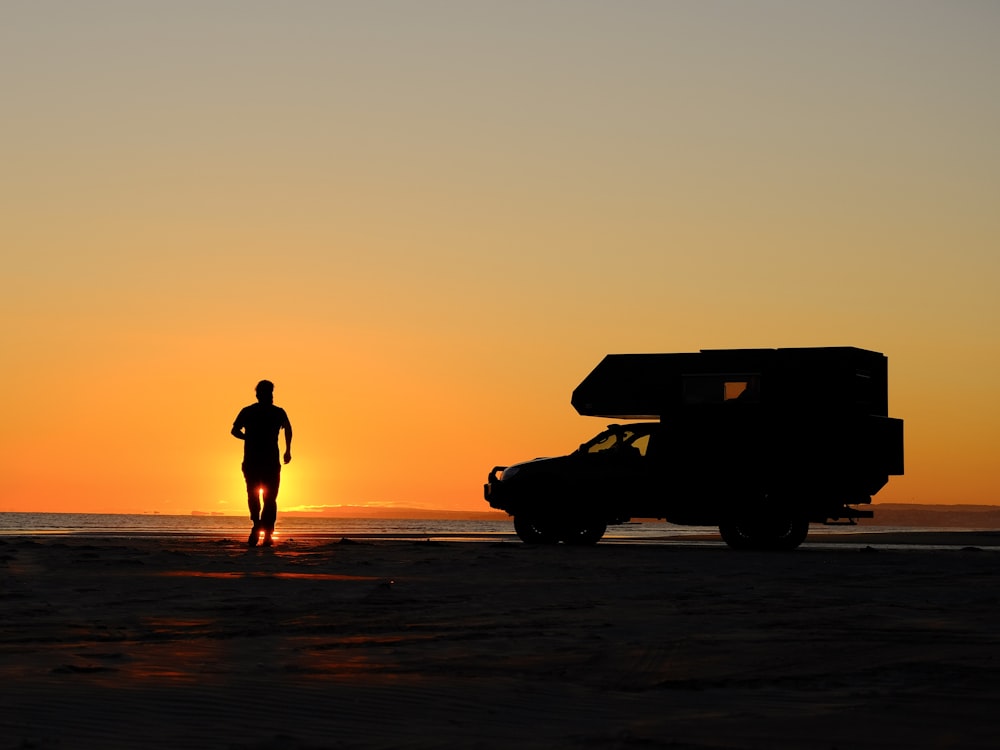a man standing on top of a sandy beach next to a truck