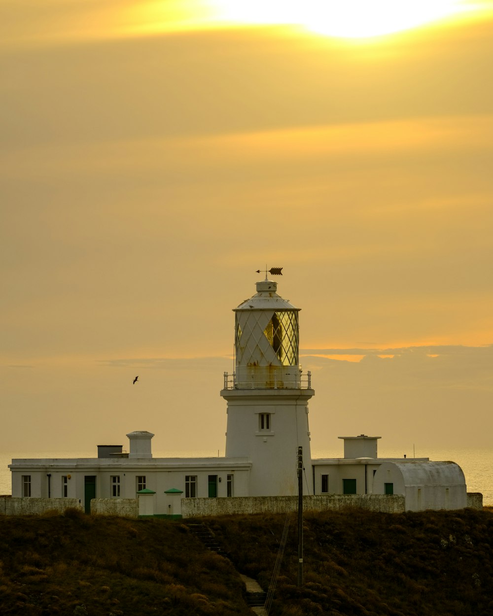 a lighthouse on a hill with the sun in the background