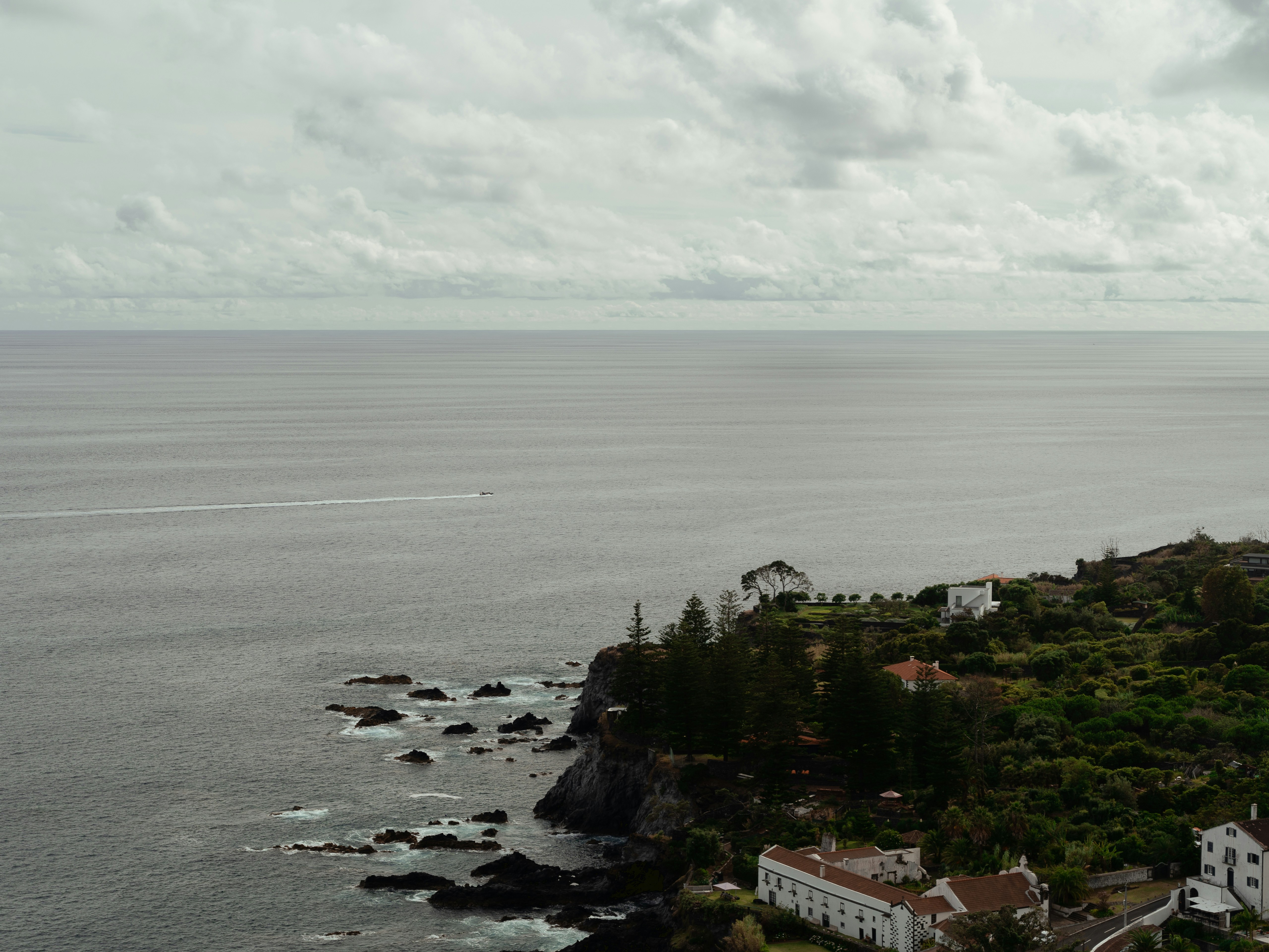 an aerial view of a house on a cliff overlooking the ocean, A boat crossing part of the atlantic ocean seen from the azores islands.