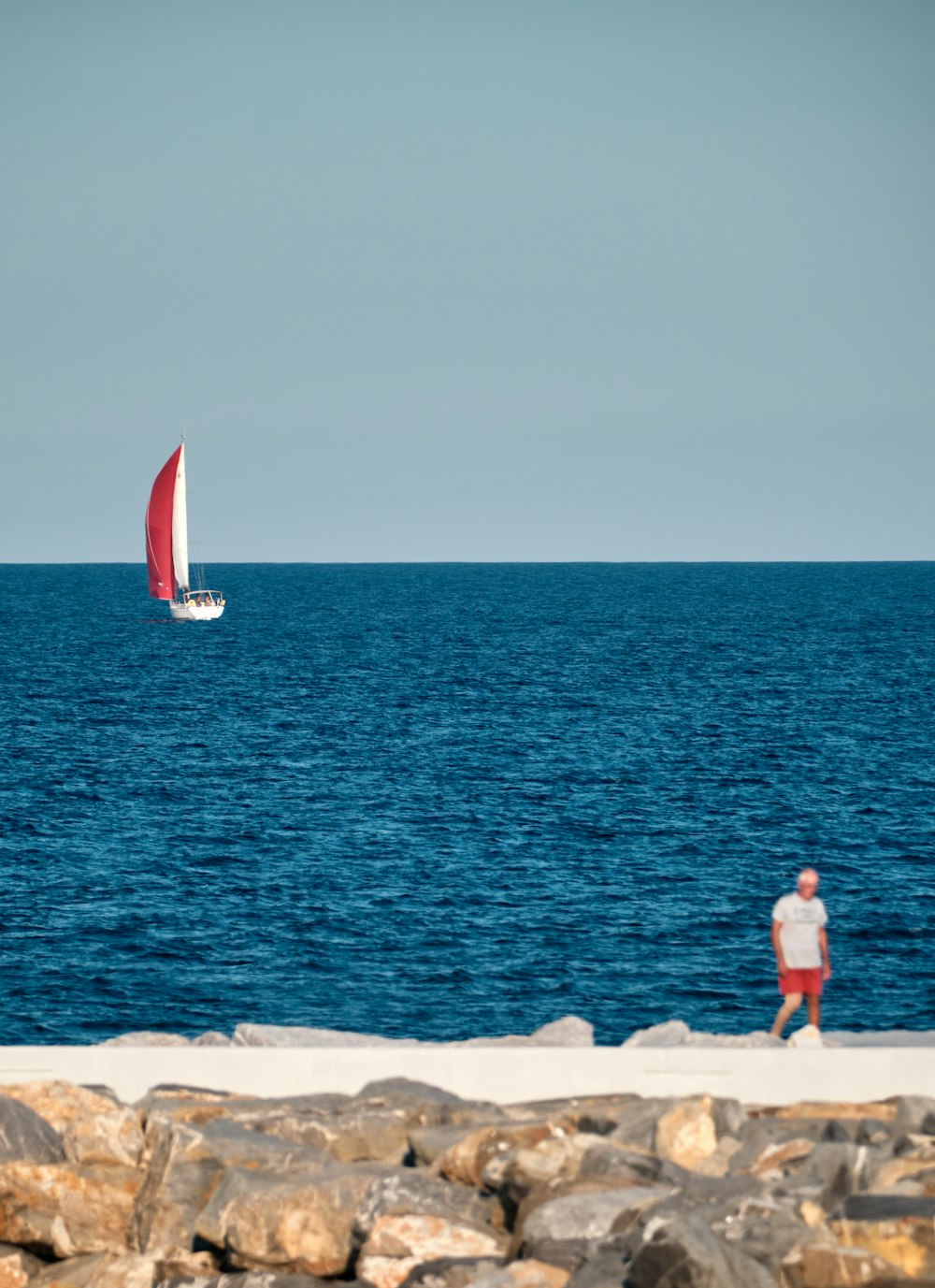 a man standing on a beach next to a sailboat