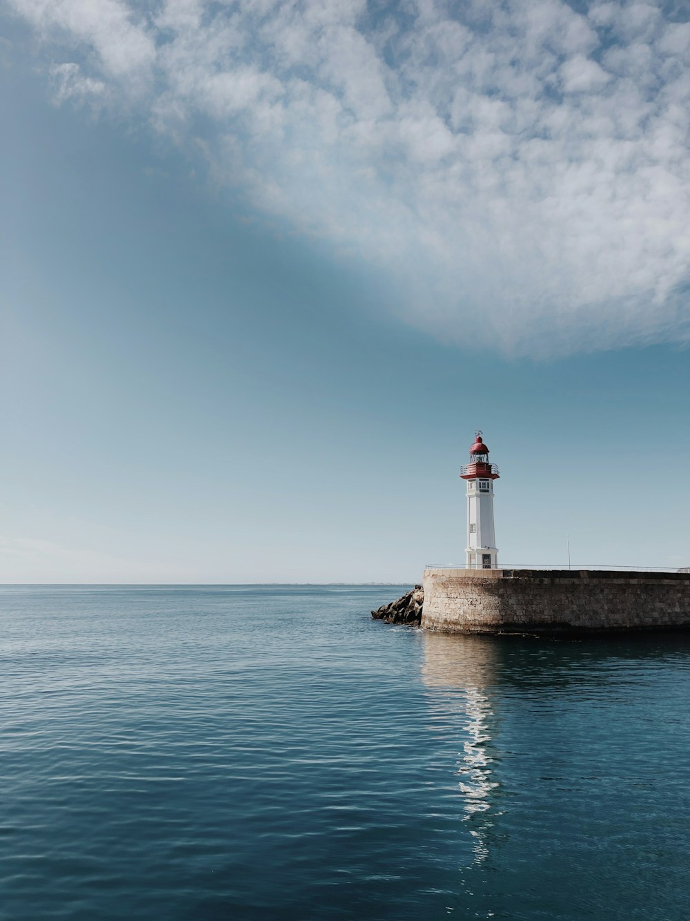 um farol sentado em cima de um píer ao lado do oceano