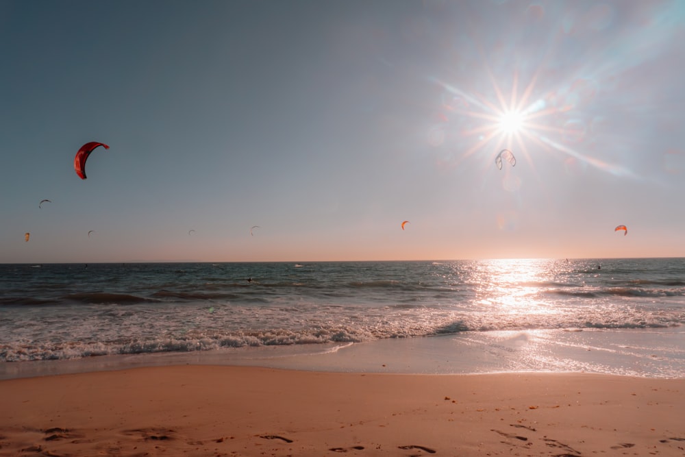 the sun is shining over the ocean with kites in the air