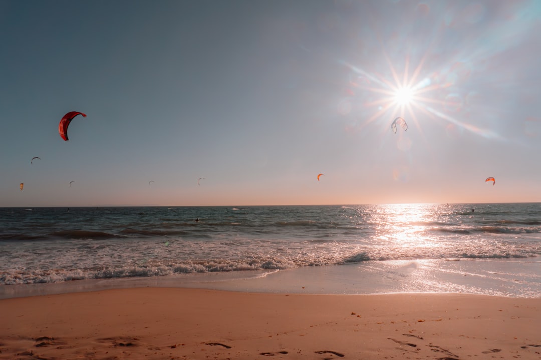 the sun is shining over the ocean with kites in the air,