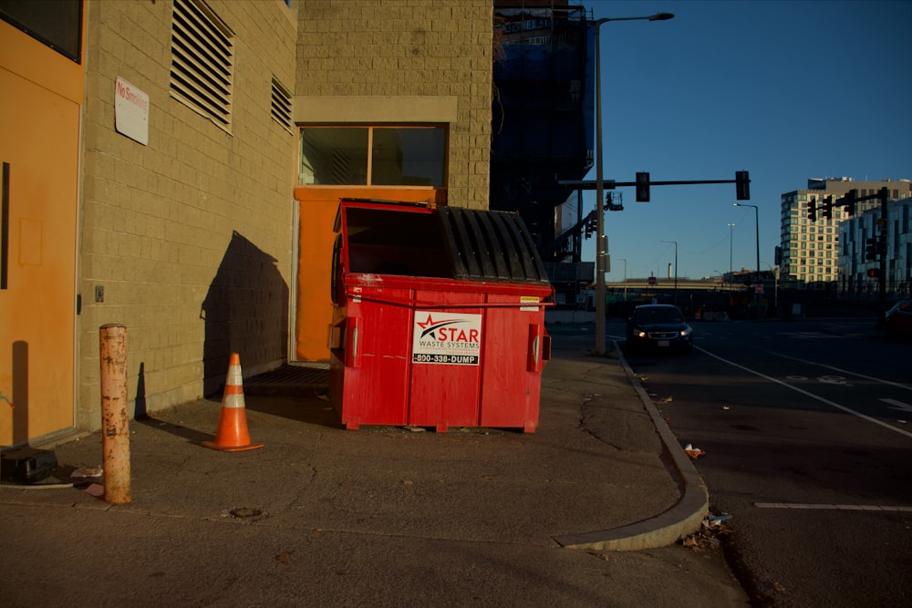 a red trash can sitting on the side of a road