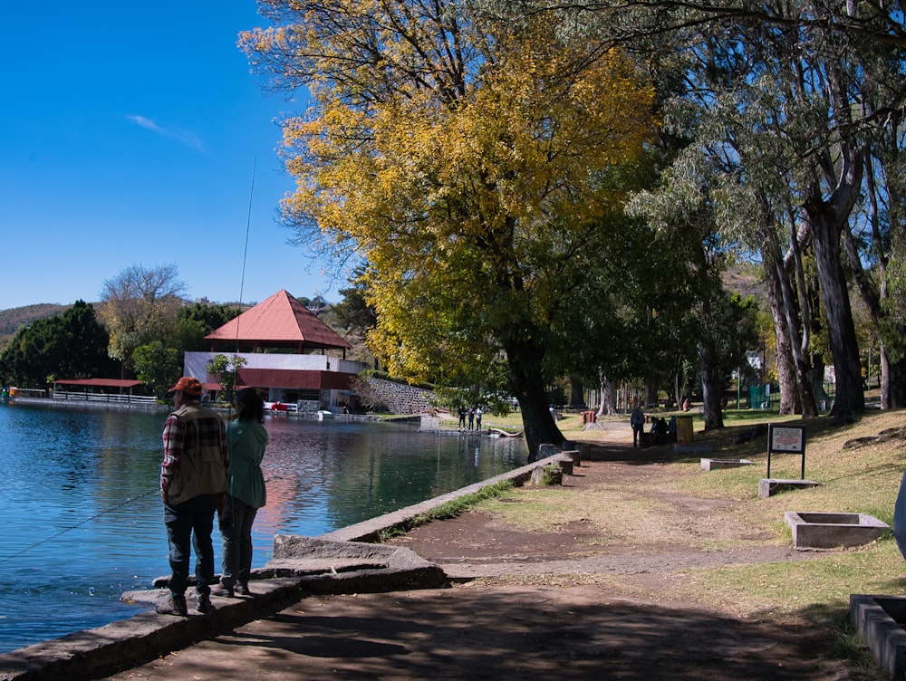 a couple of people standing on a dock next to a body of water