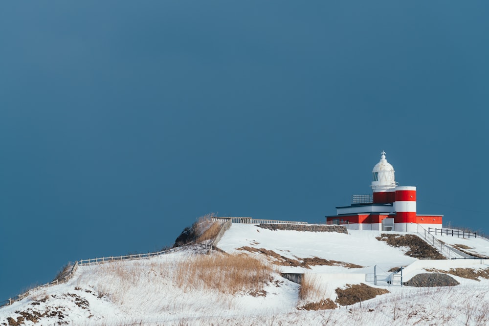 a red and white lighthouse sitting on top of a snow covered hill