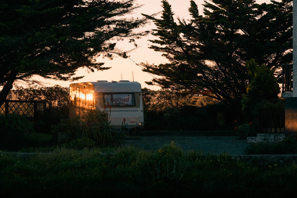 ein Wohnwagen, der bei Sonnenuntergang vor einigen Bäumen geparkt ist