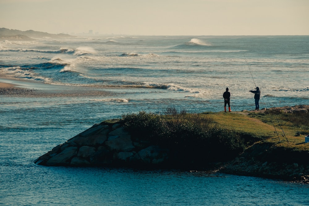 a couple of people standing on top of a hill next to a body of water