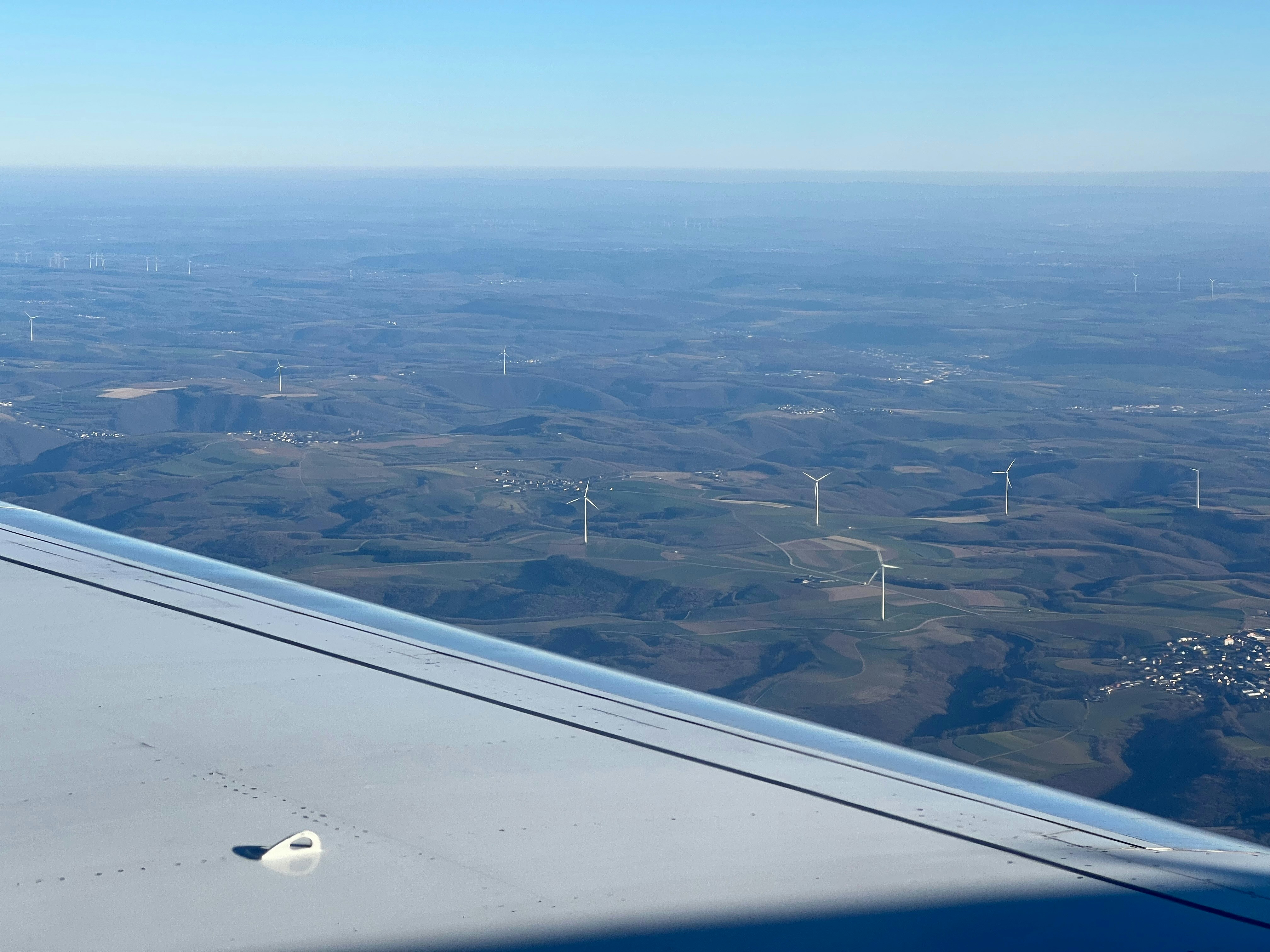 Aerial view of large wind farm with dozens of wind turbines over green hills, bright daylight, expansive blue sky