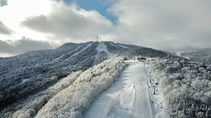 A rime-frosted groomed run and lift line climbing a mountain under low cloud