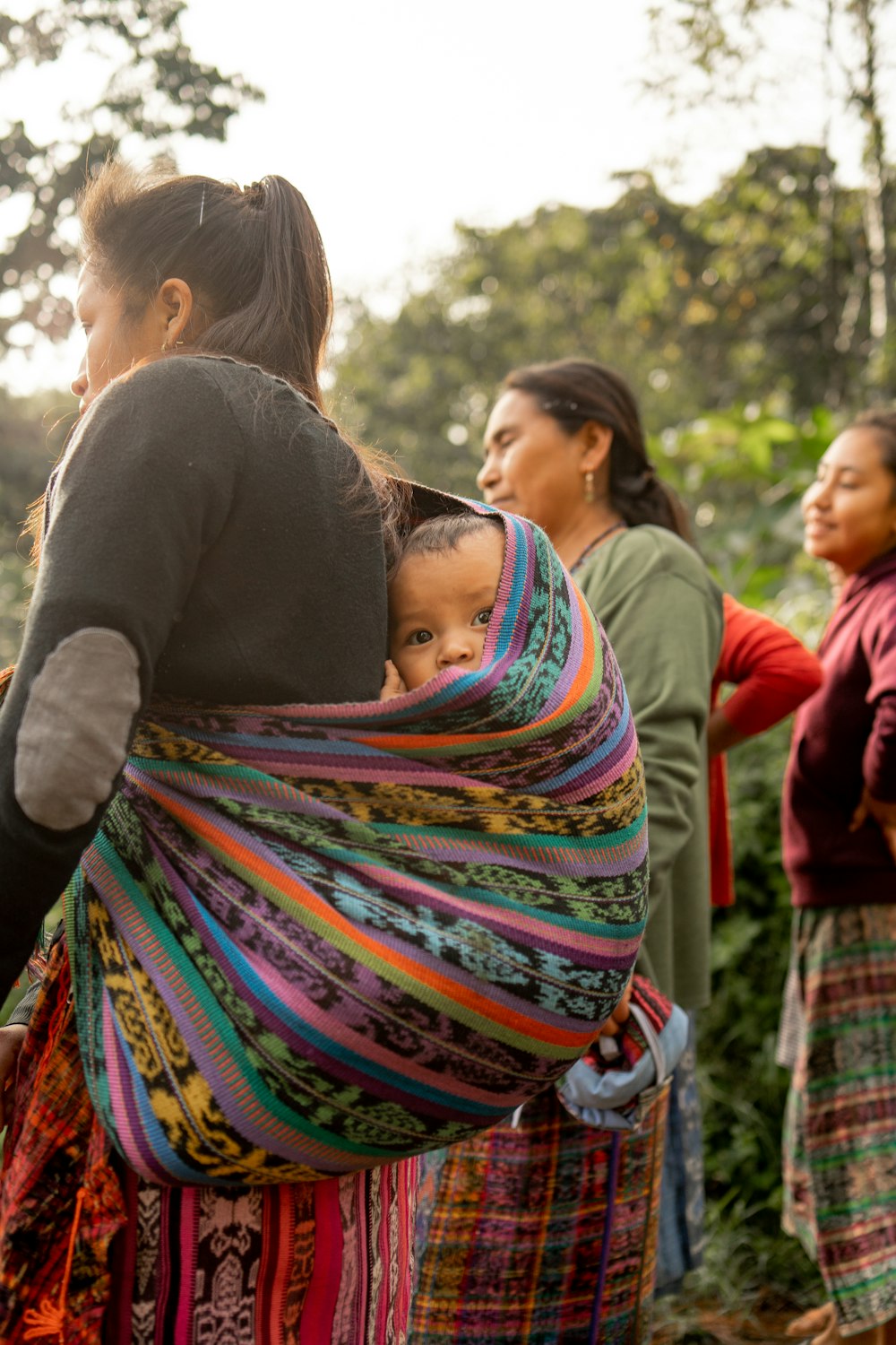 a woman carrying a child in a colorful wrap