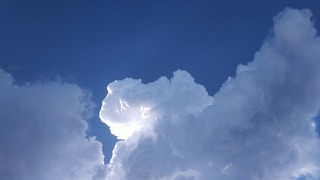 a plane flying through a cloudy blue sky