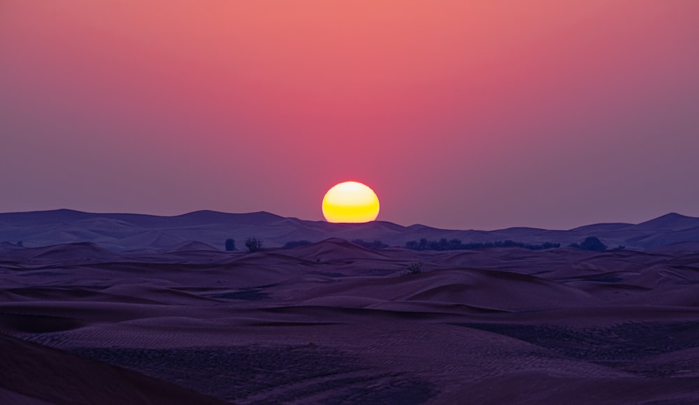 the sun is setting over a desert landscape