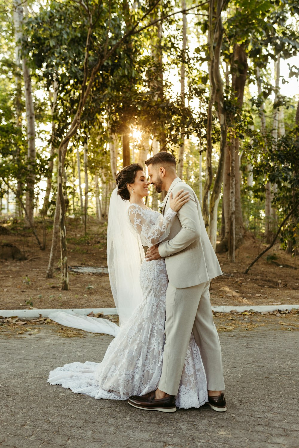 a bride and groom embracing in front of trees