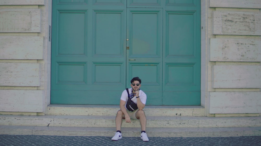 a man sitting on a step in front of a green door