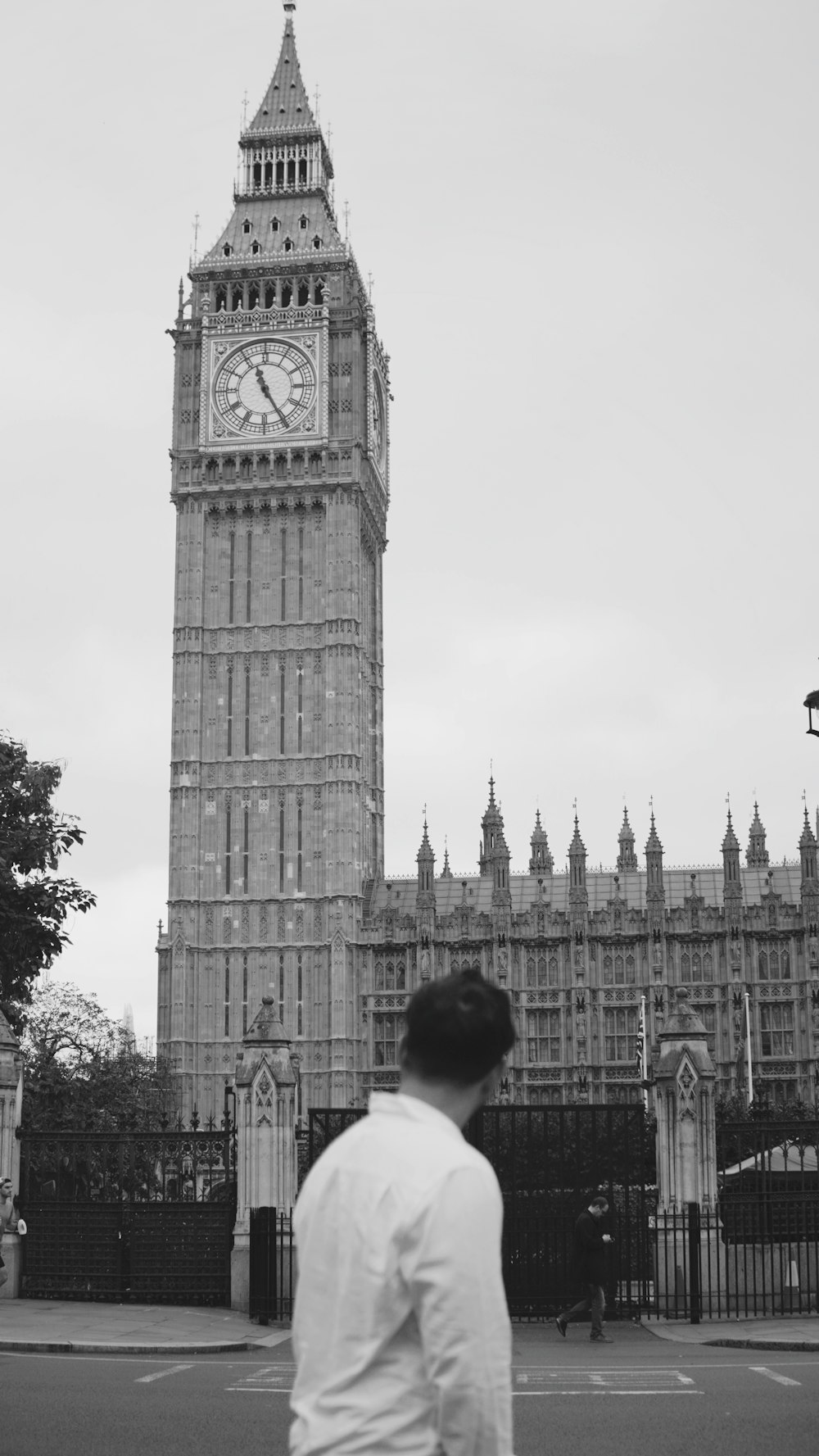 Un hombre de pie frente a una alta torre de reloj