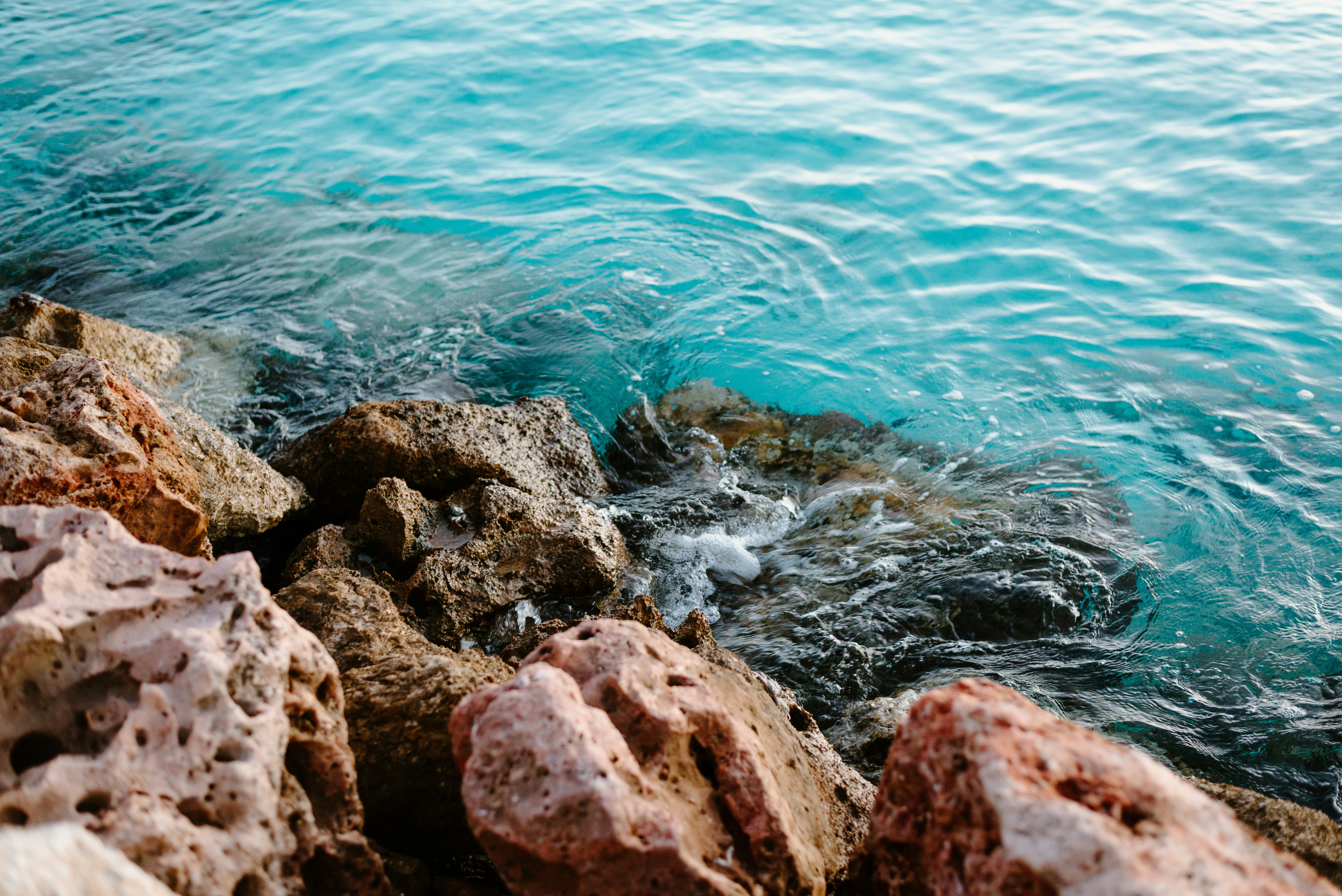 Two distinct Giorgio Armani Acqua di Giò bottles, one representing EDT and the other Profumo, placed side-by-side on a weathered stone surface near water, symbolizing their aquatic nature and contrasting depth.