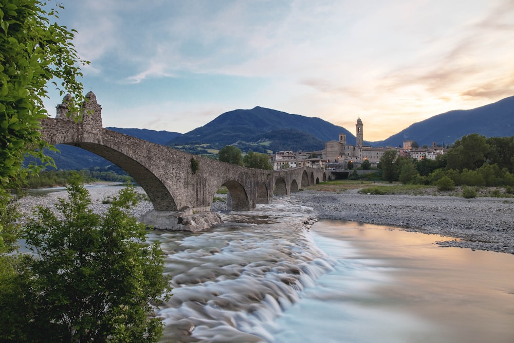 a stone bridge over a river with mountains in the background