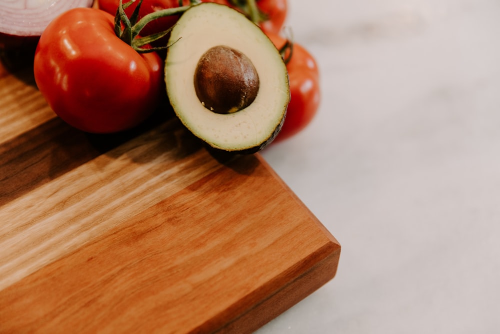 a wooden cutting board topped with sliced up tomatoes and an avocado