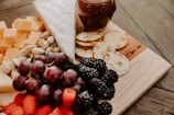 a wooden cutting board topped with cheese, fruit and crackers