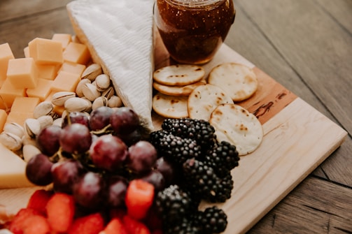a wooden cutting board topped with cheese, fruit and crackers
